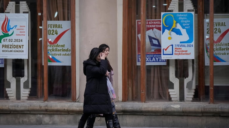 Women walk past campaign posters is in Baku, Azerbaijan, Monday,...
