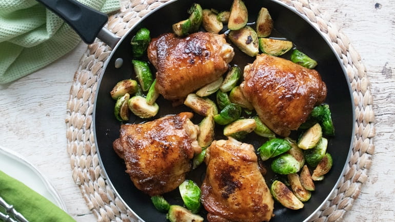 Chicken thighs and Brussels sprouts are cooked in a skillet...
