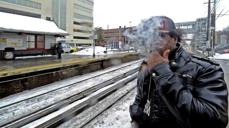 Shama Leach, of Mineola, smokes on the platform of the...