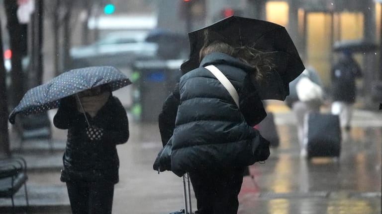 Commuters walk with umbrellas through wind-driven rain near South Station,...