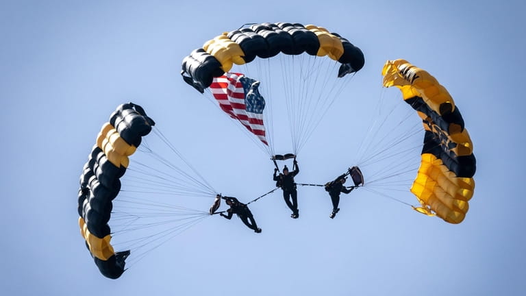 Three parachutists from the Army Golden Knights soar at the beginning...