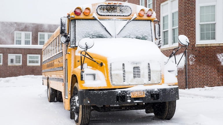 A snow-covered school bus parked beside Southold Junior-Senior High School...