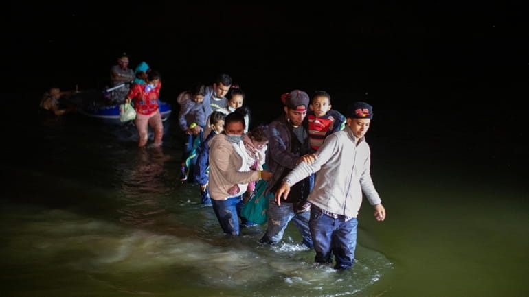 Migrant families wade through shallow waters toward Roma, Texas, March...