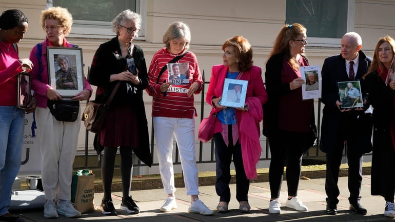 Bereaved families hold pictures of their loved ones as they...