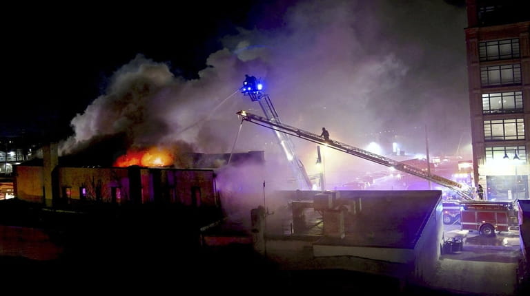 Firefighters use ladder trucks Friday evening to battle a fire...