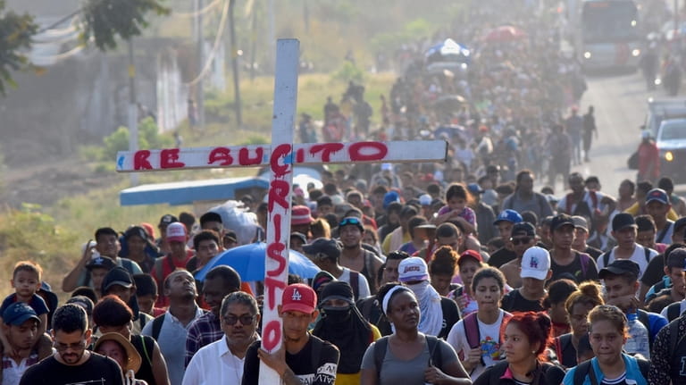 Migrants walking on the highway carry a cross that reads...