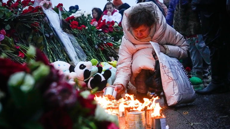 A woman lights candles at the fence next to the...