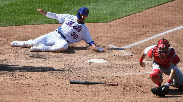 The Mets' Michael Conforto slides home behind Phillies catcher Andrew...