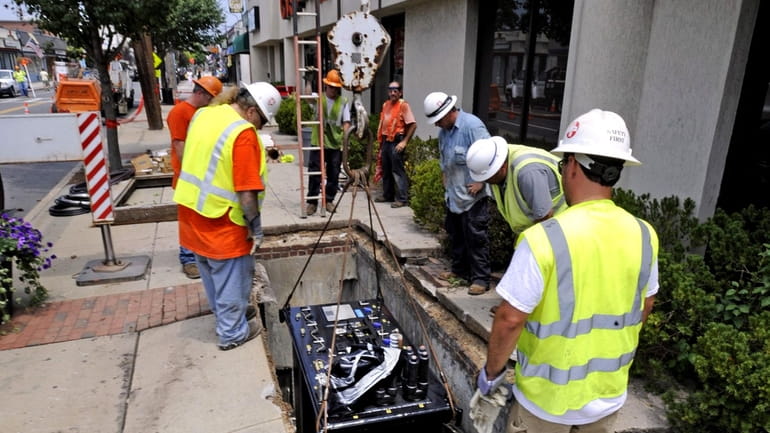 A LIPA crew lowers a new transformer under the sidewalk...