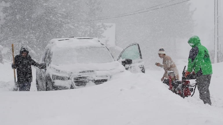 Snow falls on residents trying to clear snow during a...