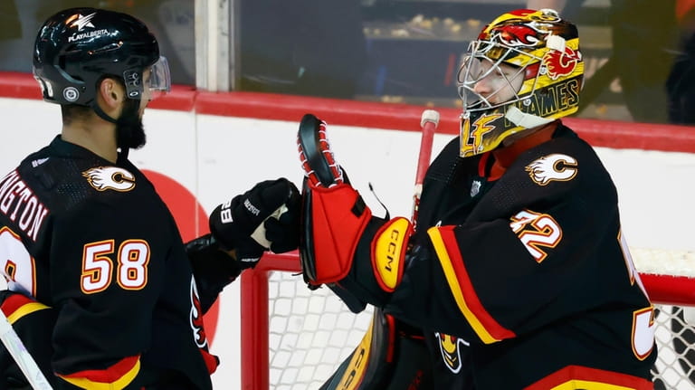 Calgary Flames goalie Dustin Wolf celebrates with Oliver Kylington after...