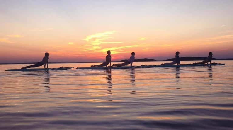 A group of stand up paddlers perform yoga on their...