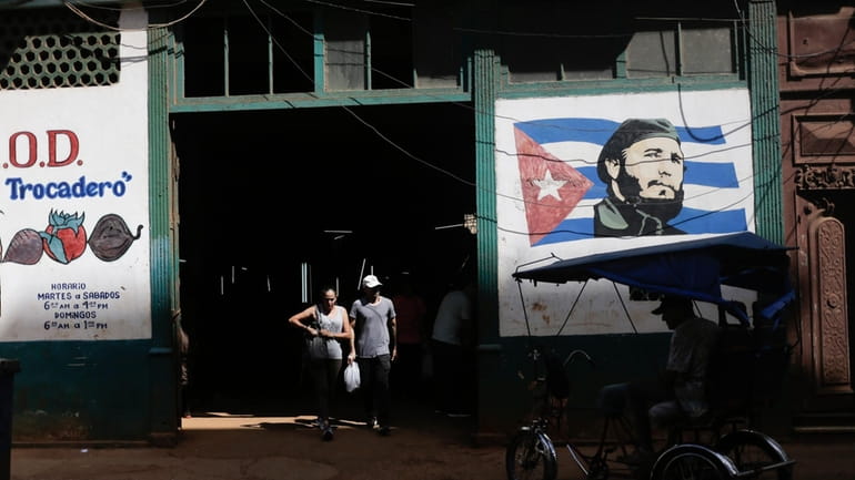 Shoppers exit a state-run agro-market, where a mural of Fidel...