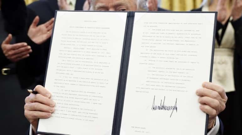 President Donald Trump holds up a signed executive order in...