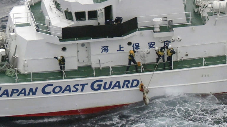 Japanese coast guard members pick up a floating object as...