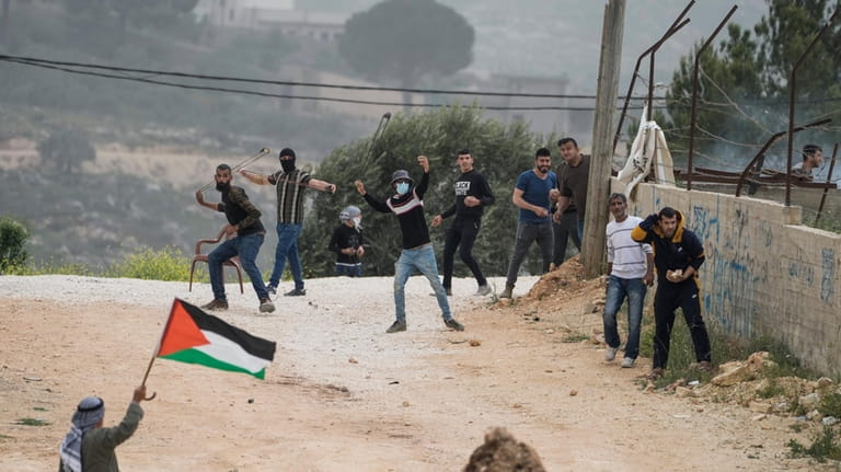 Palestinians hurl stones and wave a Palestinian flag toward Israeli...