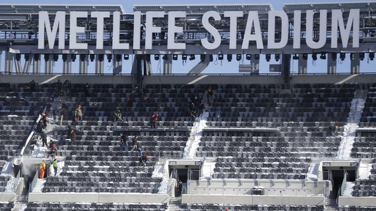 Workers shovel snow off the seats at MetLife Stadium as...