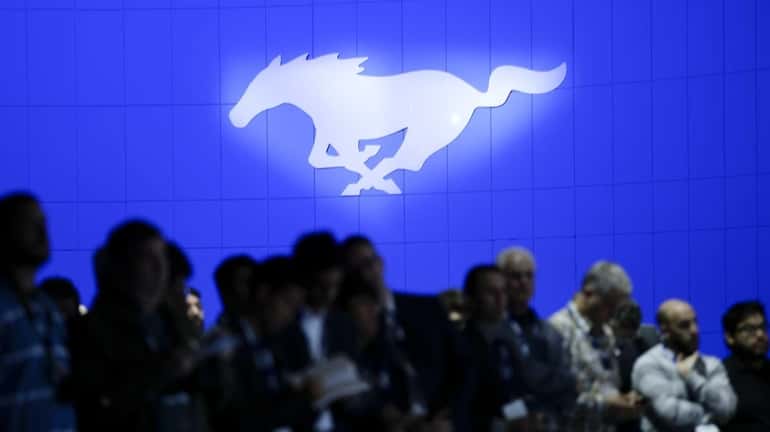 The Ford Mustang logo is displayed behind people gathering for...