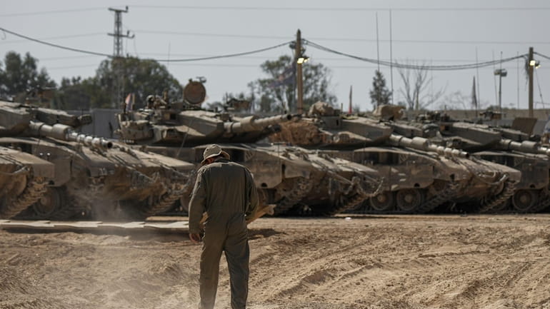 Israeli soldiers work on tanks at a staging ground near...