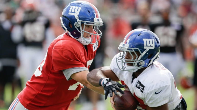 New York Giants quarterback Eli Manning, left, hands the ball...