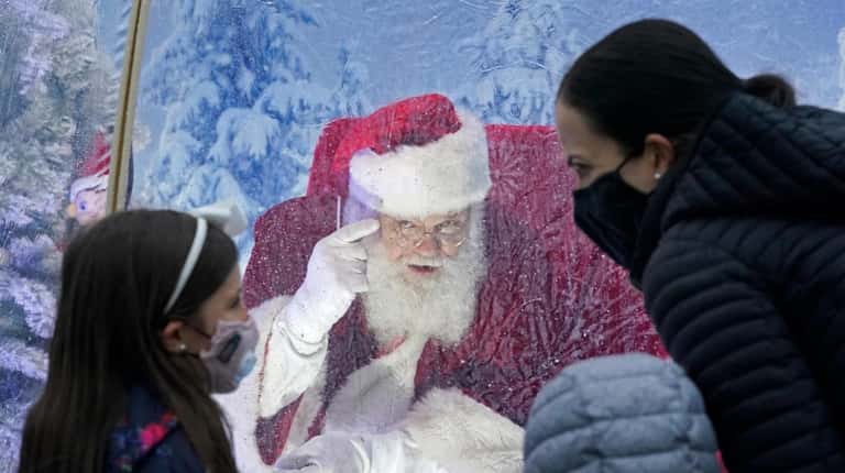 Santa, portrayed by Dan Kemmis, talks to a family wearing...