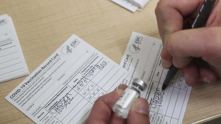 A healthcare worker fills out a COVID-19 Vaccination Record Card...