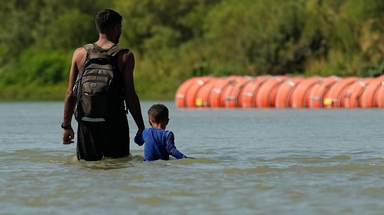 Migrants walk past large buoys being used as a floating...