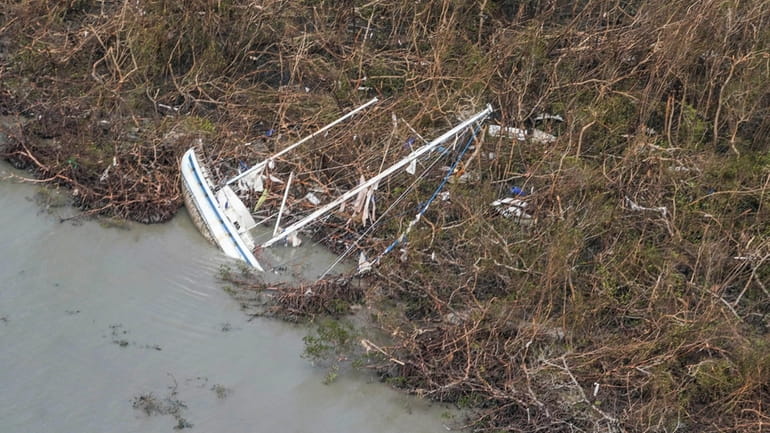 A damaged sailboat lies in water in the aftermath of...