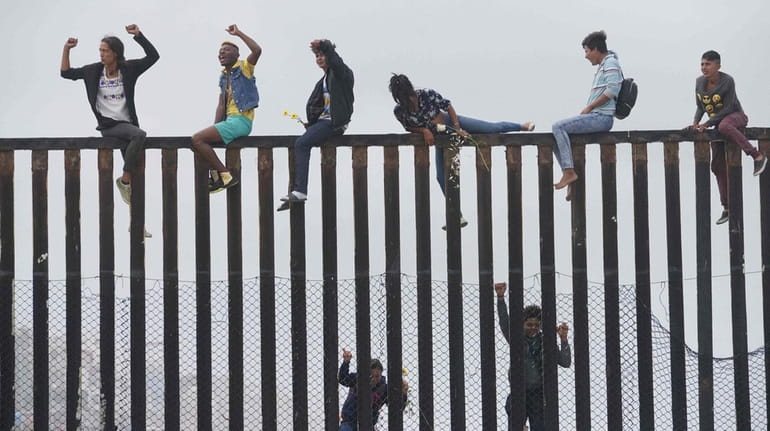 Migrant caravan demonstrators climb the US-Mexico border fence during a...