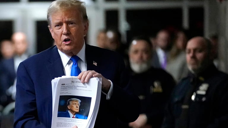 Former President Donald Trump holds up news clippings as he...
