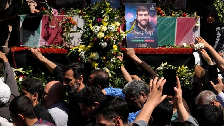 Iranian mourners try to touch the flag-draped coffins of Revolutionary...