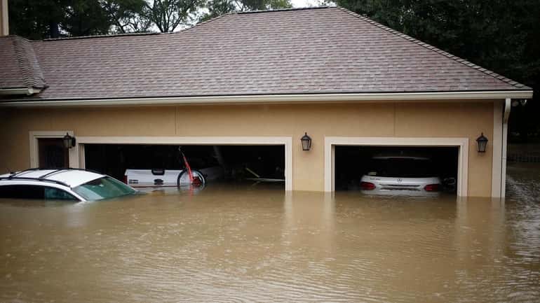 A house and vehicles stand in Harvey's floodwaters in Spring,...