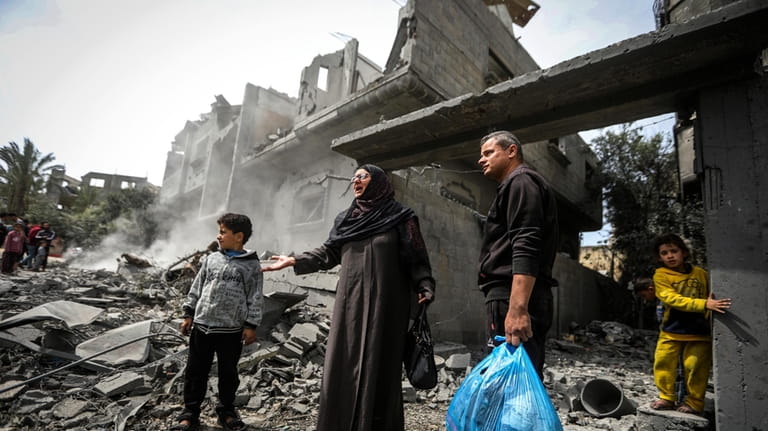 Palestinians collect their belongings from the rubble of a residential...