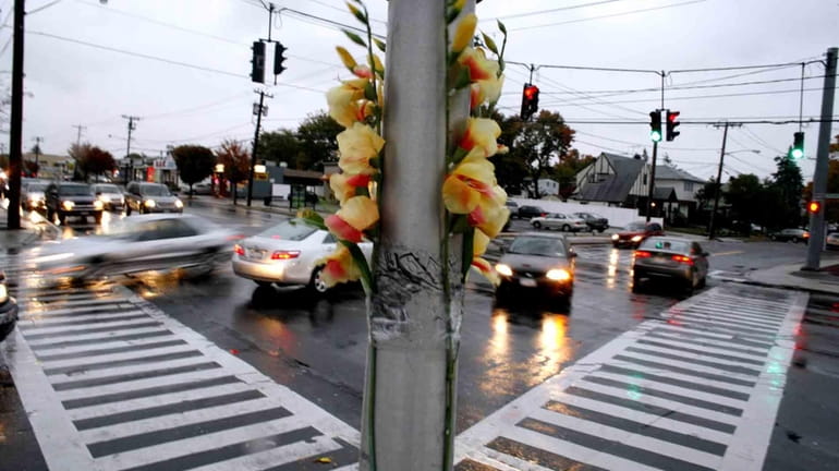 Flowers are taped to a pole at the intersection of...