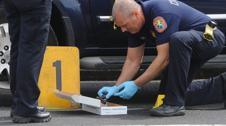 A Nassau County crime scene investigator inspects a gun dropped...
