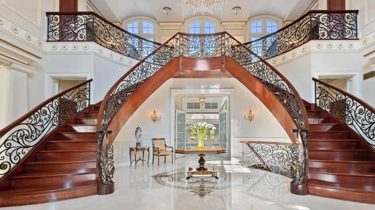 The foyer has a marble floor and double staircase with wrought-iron...