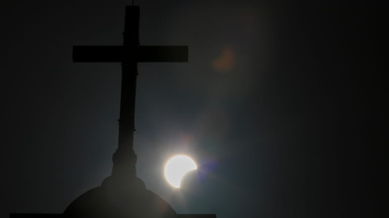 A partial solar eclipse is seen behind a cross on...