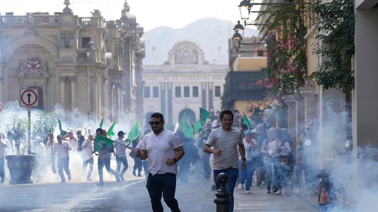 People run for cover as police launch tear gas to...