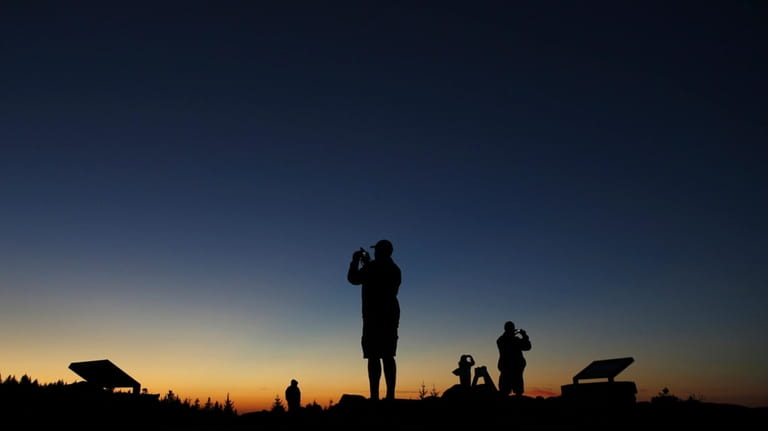 Tourists photograph the sunset at the summit of Cadillac Mountain...
