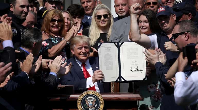 President Donald Trump shows off his signature on the bill to...