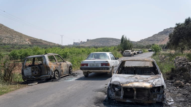 Torched vehicles are seen along the road in the West...