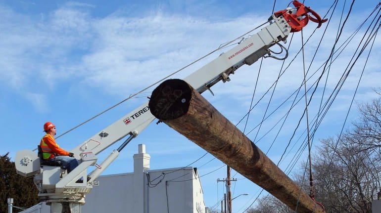 Workers plant a new utility pole at the intersection of...