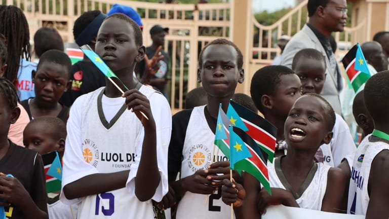 South Sudanese hold flags as they wait to welcome back...