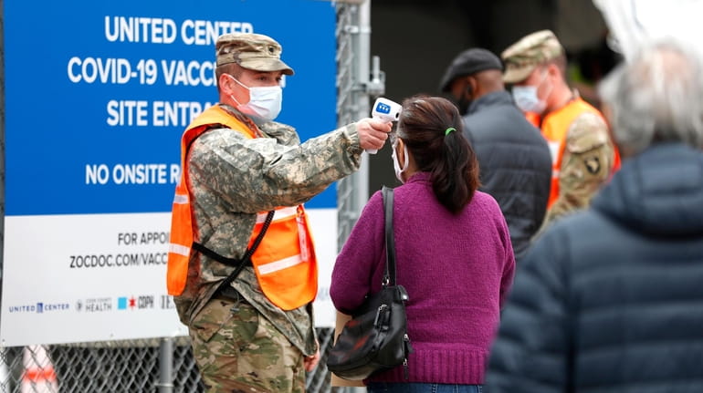 A National Guard member checks the temperature of people entering...