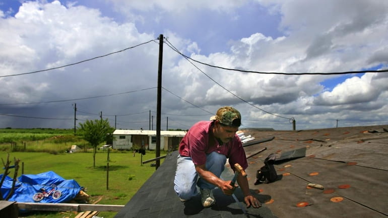 Jose Garcia hammers down roof shingles on his home as...