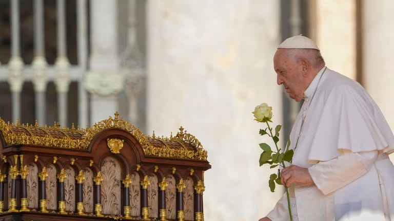 Pope Francis brings a rose before praying in front of...