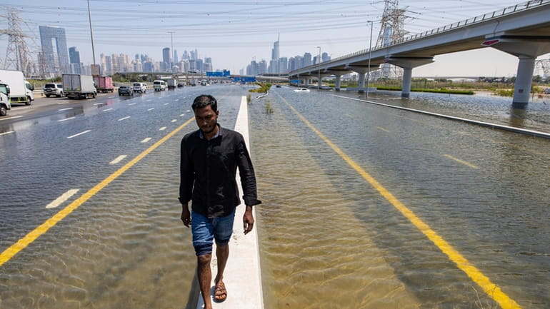 A man walks along a road barrier among floodwater caused...