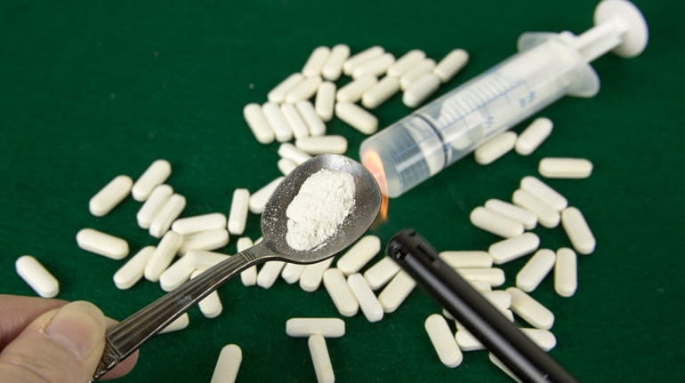 Crushed powdered opioids in spoon with lighter, pills and syringe.