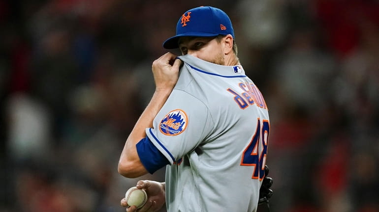 Mets starting pitcher Jacob deGrom wipes his face after allowing...