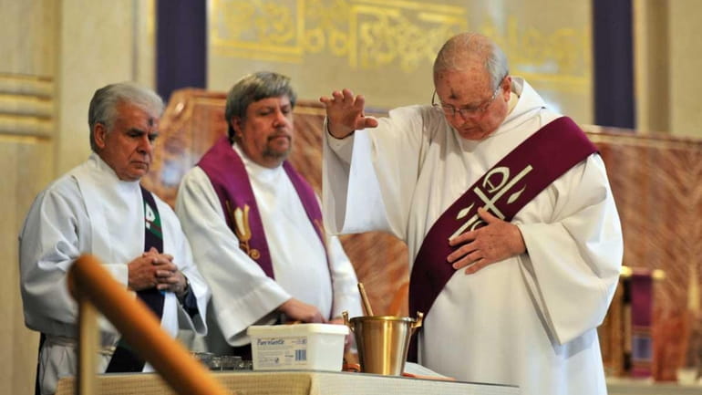 Deacon Robert Campbell, right, blesses ashes before distributing them to...